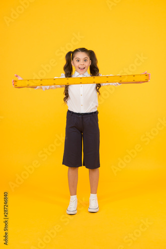 What a long ruler. Surprised little student holding rigid wooden ruler on yellow background. Small child taking measurements with metric ruler. My ruler is one meter long