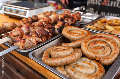A counter with metal trays containing grilled sausages and meat. Food and cooking equipment at a street food festival