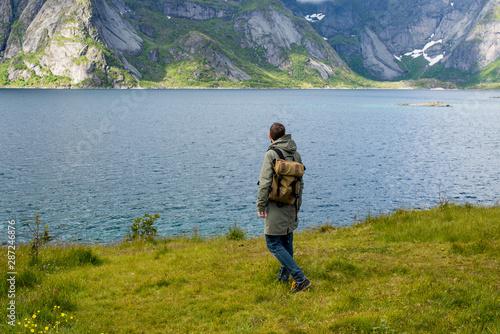 A man with a backpack looks at the fjord. Beautiful nature landscape in North. Amazing scenic outdoor view. Enjoy the moment, relaxation. Wanderlust. Travel, adventure, lifestyle. Explore Norway