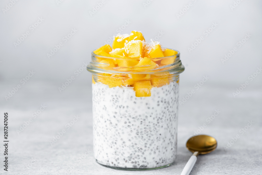 Chia seed pudding with mango and coconut in glass jar on bright grey concrete background. Healthy food, clean eating dieting vegan lifestyle concept - obrazy, fototapety, plakaty 