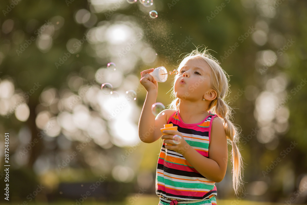 little blonde girl inflates soap bubbles in summer on a walk, International children's day little blonde girl inflates soap bubbles in summer on a walk, International children's day