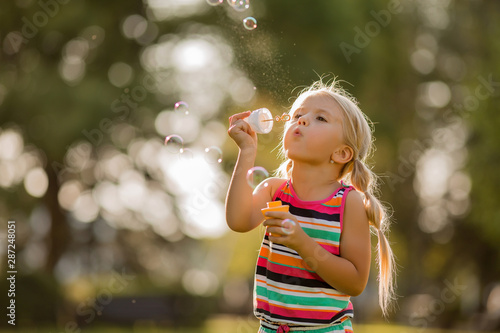 little blonde girl inflates soap bubbles in summer on a walk, International children's day