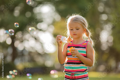 little blonde girl inflates soap bubbles in summer on a walk   International children s day