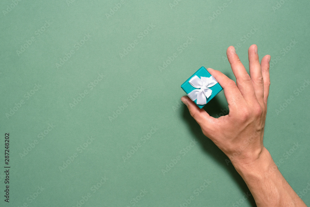Small gift box in the male hand on green background with copy space.