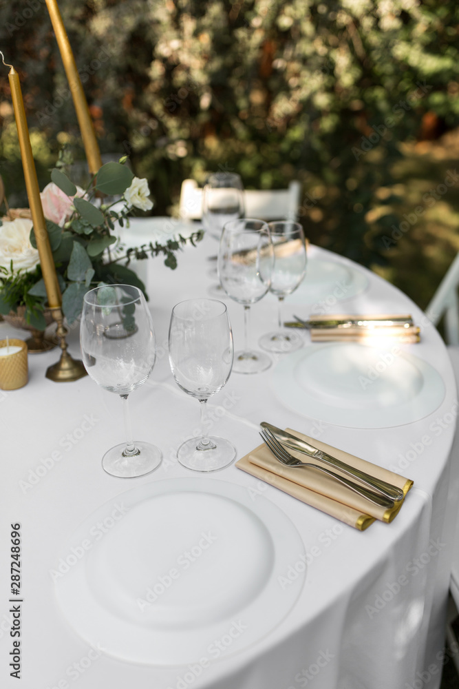 Wedding table setting decorated with fresh flowers in a brass vase. Wedding floristry. Banquet table for guests outdoors with a view of green nature. Bouquet with roses, eustoma and eucalyptus leaves Wedding table setting decorated with fresh flowers in a brass vase. Wedding floristry. Banquet table for guests outdoors with a view of green nature. Bouquet with roses, eustoma and eucalyptus leaves