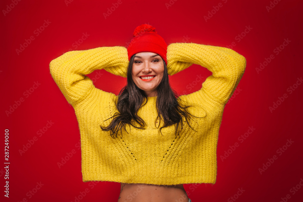 A girl in a yellow sweater and a hat on a red background grimaces A girl in a yellow sweater and a hat on a red background grimaces