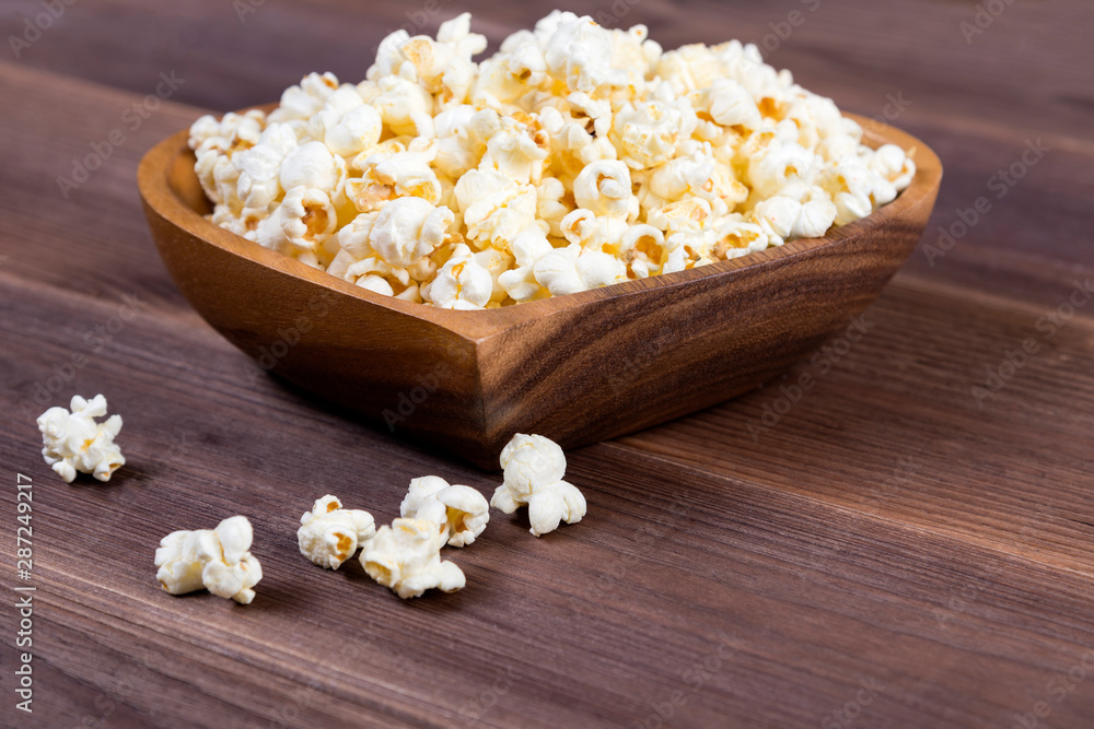 Popcorn in a brown wooden plate in the shape of a heart on a wooden table. Popcorn is laid out on the table Popcorn in a brown wooden plate in the shape of a heart on a wooden table. Popcorn is laid out on the table