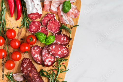 Meat antipasto platter. Salami, sliced ham, sausage, bacon with vegetables and herbs on white marble table. top view