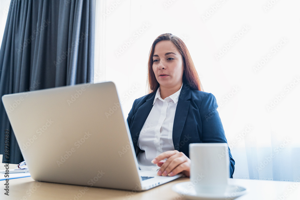 Young attractive caucasian woman smiling and making video call or online chat, looks at web camera of laptop. Distant teacher or coach, or tutor of online school or internet friend Young attractive caucasian woman smiling and making video call or online chat, looks at web camera of laptop. Distant teacher or coach, or tutor of online school or internet friend