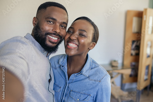 Smiling young African American couple taking a selfie at home