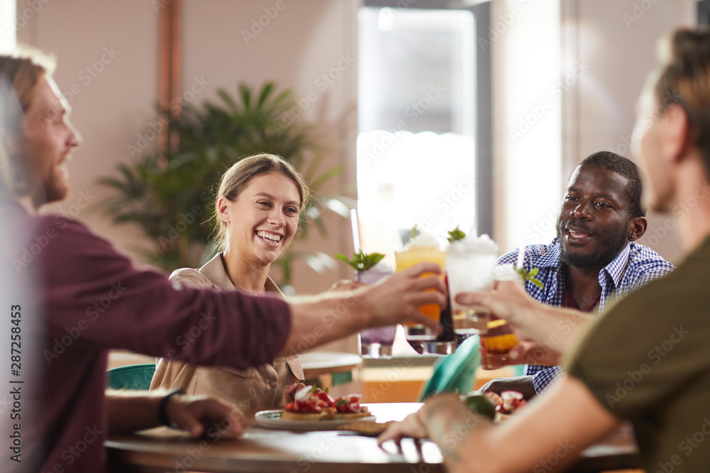 Multi-ethnic group of friends clinking glasses while sitting at table in cafe enjoying cold refreshing drinks, copy space Multi-ethnic group of friends clinking glasses while sitting at table in cafe enjoying cold refreshing drinks, copy space