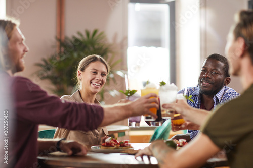 Multi-ethnic group of friends clinking glasses while sitting at table in cafe enjoying cold refreshing drinks  copy space