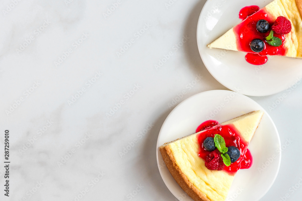 two slices of New York cheesecake in plates with fresh berries, jam and mint on white marble table. top view two slices of New York cheesecake in plates with fresh berries, jam and mint on white marble table. top view