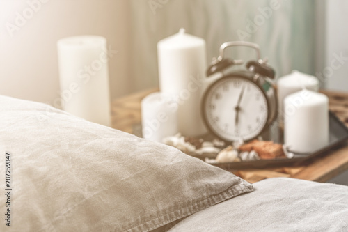 Cozy gray bedroom interior with comfortable bed near the wooden night table with candle, alarm clock and dried flowers. Cozy atmosphere at home. Warming up autumn evenings. Vintage furniture.