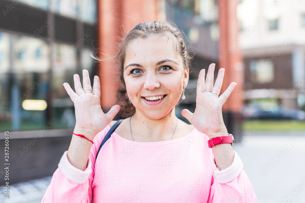 Portrait of enthusiastic young Caucasian woman raising her hands up on the street.