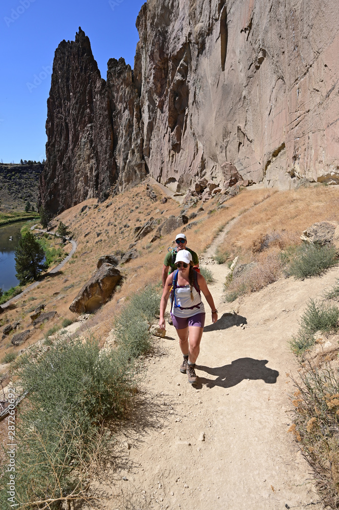 Obraz premium Young couple ascend Misery Ridge Trail in Smith Rock State Park, Oregon on a cloudless summer day.