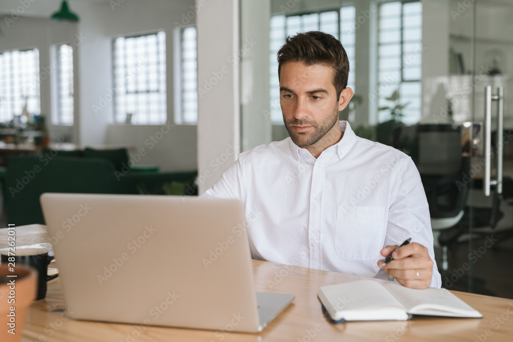 Young businessman writing down notes while working on a laptop Young businessman writing down notes while working on a laptop