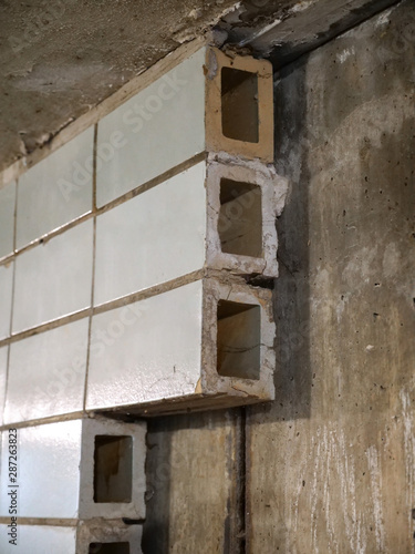 Close up of the ends of glazed clay hollow block tiles where several are missing showing the concrete substrate at a pedestrian underpass below a bridge in Chicago.