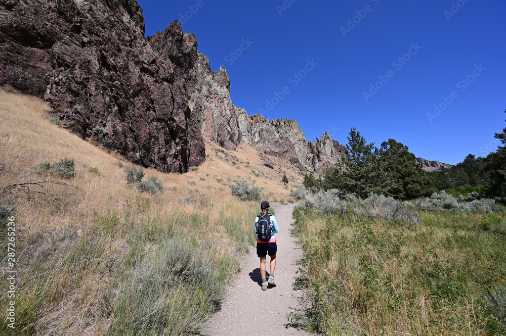 Woman hikes and photographs Misery Ridge Trail in Smith Rock State Park near Terrebonne, Oregon on cloudless summer day.