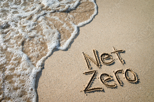 Net Zero message for energy consumption handwritten on smooth sand beach with oncoming wave  photo