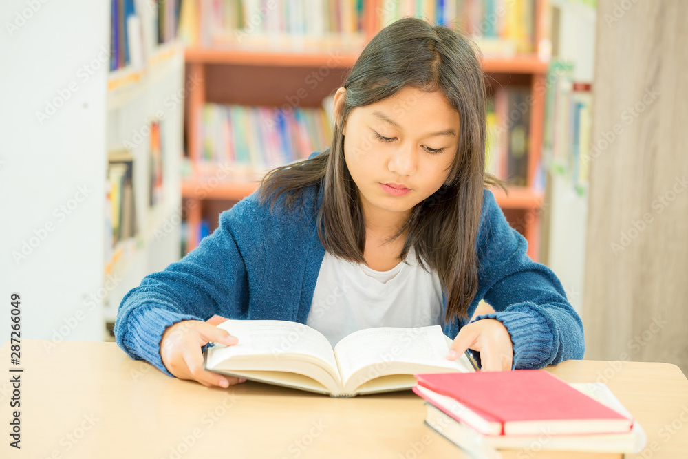 Portrait of clever student with open book reading it in college library Portrait of clever student with open book reading it in college library