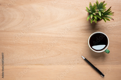 Wooden office desk table with cup of black coffee, pen and plant pot. Top view with copy space, flat lay.
