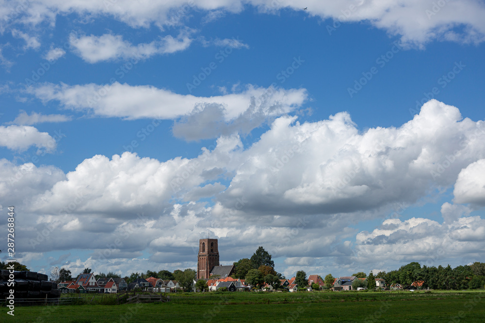 Small village of Ransdorp near Amsterdam rising from the agrarian green pasture fields with dramatic clouds in the blue sky above