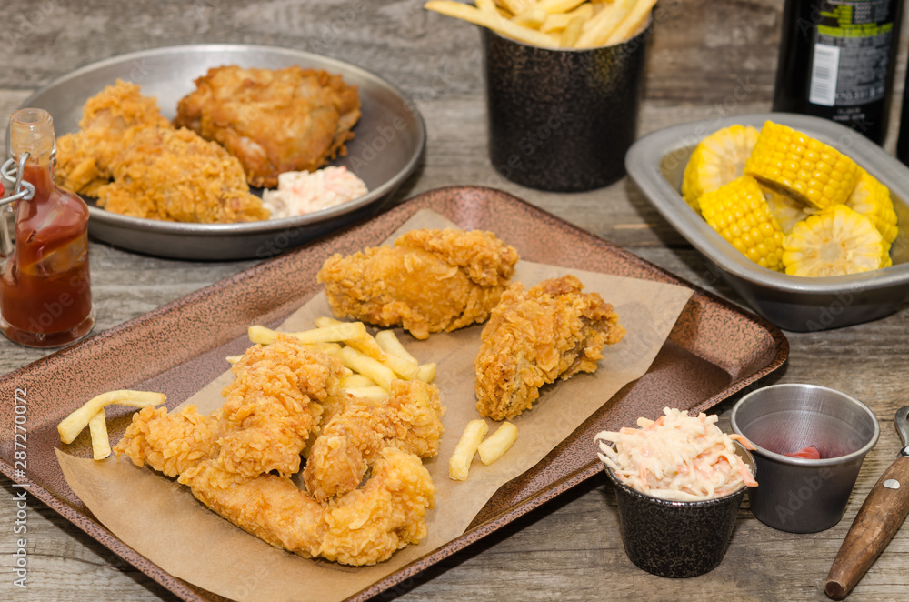Dinner table with fried chicken, wings and strips, french fries, coleslaw and sauces. Homemade southern fried chicken. Dinner table with fried chicken, wings and strips, french fries, coleslaw and sauces. Homemade southern fried chicken.