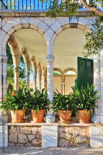 Exterior of the terrace of an old building with columns, arches and pots with plants in the sunlight. Spain