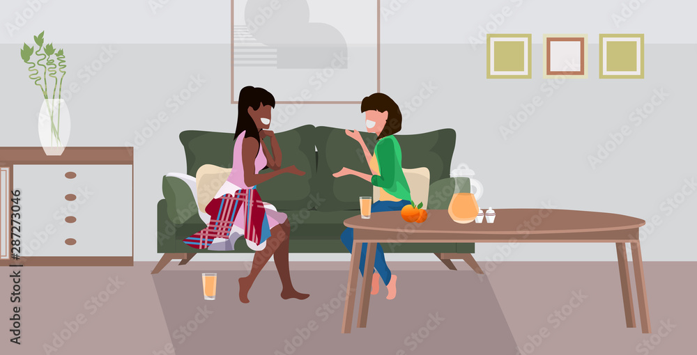 Fototapeta premium two girls sitting on couch mix race women couple discussing during meeting modern living room interior flat full length horizontal