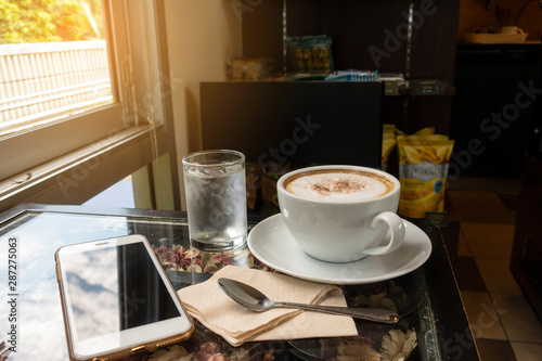 The ceramic cup of hot cappuccino coffee on the wooden table in the restaurant or coffee shop. natural light. morning hot drink cafe shop.