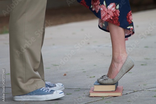 young man and woman standing facing each other with only legs and shoes visible girl on tip toes on books