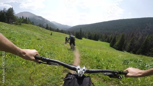 Three People Mountain Biking Through Meadow Of Flowers On A Sunny Day