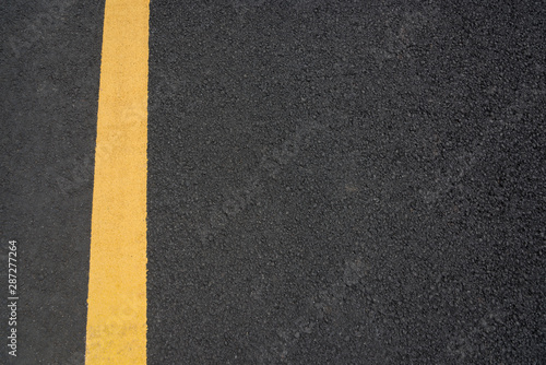 A vertical yellow paint line on black asphalt texture top view text space