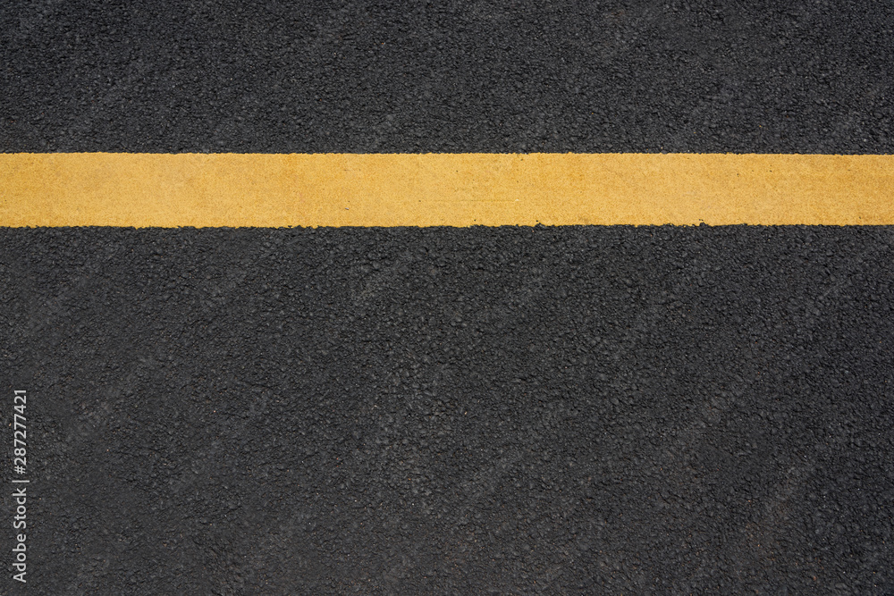 A parallel yellow paint line close-up text space on black asphalt road A parallel yellow paint line close-up text space on black asphalt road