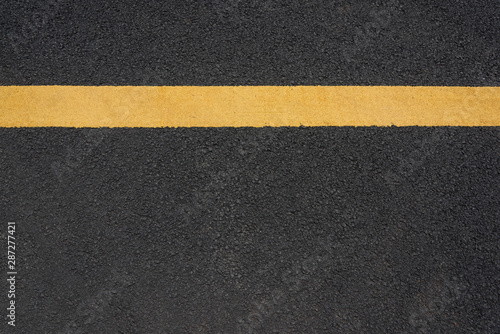 A parallel yellow paint line close-up text space on black asphalt road