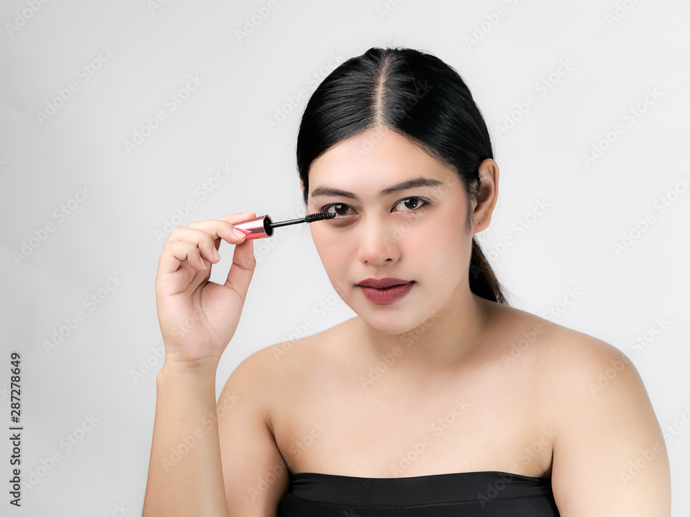 Close-up portrait of nice lovely cute sweet attractive cheerful positive Asian woman holding in hands applying trendy black mascara isolated over gray background. Close-up portrait of nice lovely cute sweet attractive cheerful positive Asian woman holding in hands applying trendy black mascara isolated over gray background.