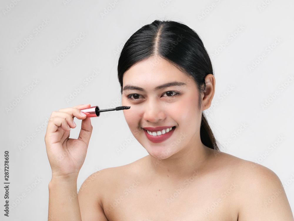 Close-up portrait of nice lovely cute sweet attractive cheerful positive Asian woman holding in hands applying trendy black mascara isolated over gray background. Close-up portrait of nice lovely cute sweet attractive cheerful positive Asian woman holding in hands applying trendy black mascara isolated over gray background.