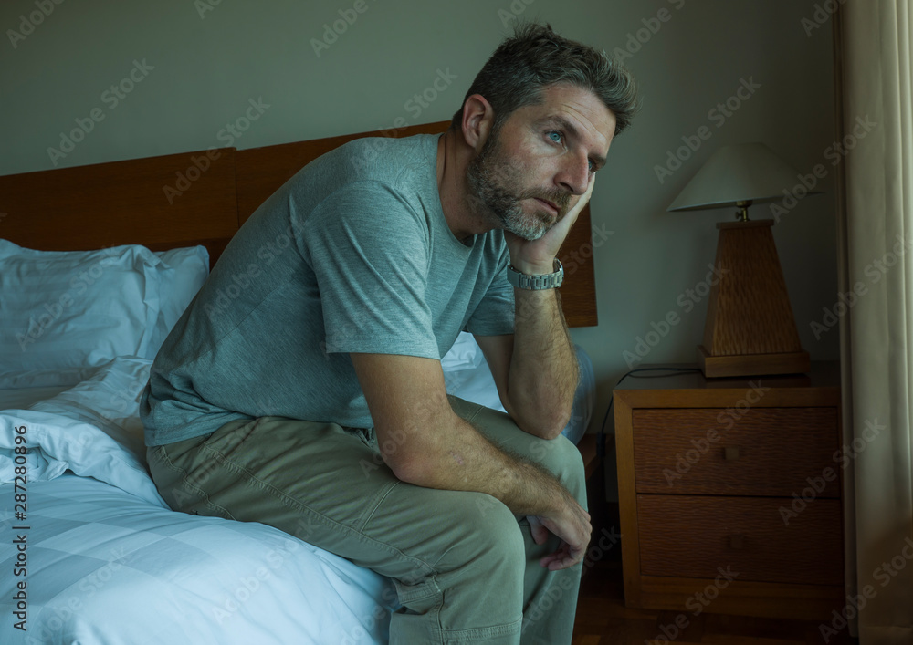dramatic lifestyle portrait of handsome guy sitting on bed feeling sad thinking and suffering depression and anxiety problem dramatic lifestyle portrait of handsome guy sitting on bed feeling sad thinking and suffering depression and anxiety problem