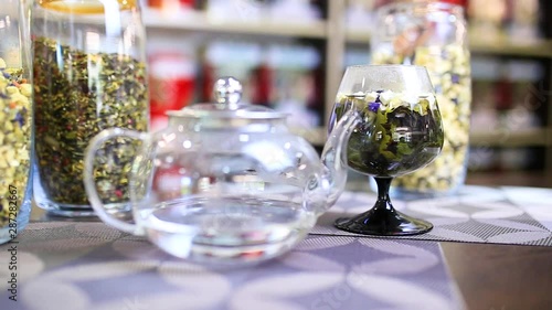 Blue loose tea in the tall glass. Teapot with hot water.