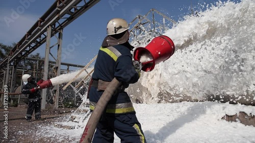 Three firefighters extinguish a fire at a tank farm with foam