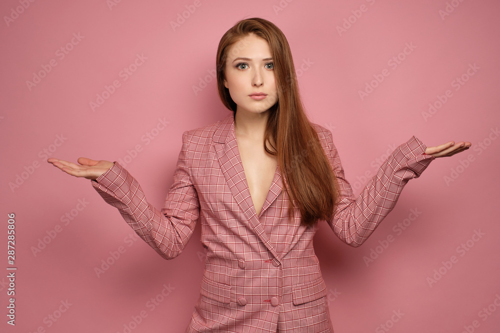 Redhead girl in a jacket stands on a pink background with arms outstretched to the sides and wide-open eyes looking at the camera Redhead girl in a jacket stands on a pink background with arms outstretched to the sides and wide-open eyes looking at the camera