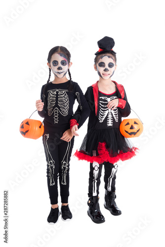 Full length of two asian girls in skeleton costume holding halloween pumpkin bucket and smiles over white background