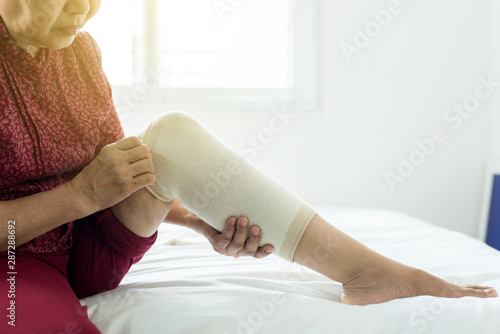 Fototapet Senior asian woman using elastic bandage on injured knee