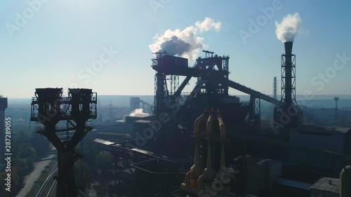 Aerial view over industrialized city with air atmosphere and river water pollution from metallurgical plant. Dirty smoke and smog from pipes of steel factory and blast furnaces. Ecological