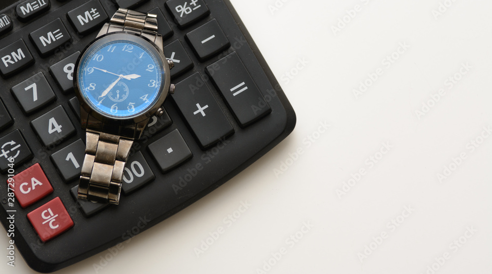 A wristwatch lies on a black calculator. Objects are placed on a white background. Concept - time to submit a report, accountant, count, time to work. Copy space A wristwatch lies on a black calculator. Objects are placed on a white background. Concept - time to submit a report, accountant, count, time to work. Copy space