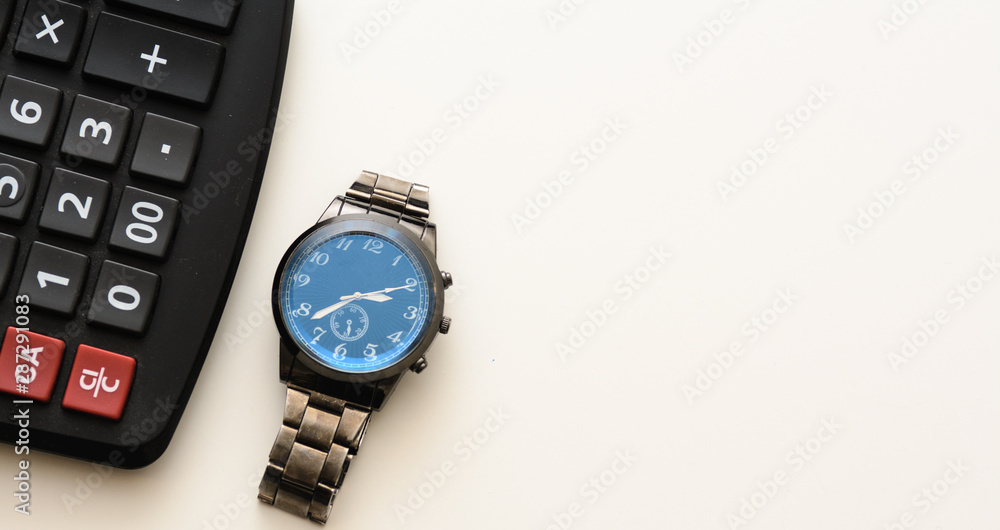 A wristwatch lies on a black calculator. Objects are placed on a white background. Concept - time to submit a report, accountant, count, time to work. Copy space A wristwatch lies on a black calculator. Objects are placed on a white background. Concept - time to submit a report, accountant, count, time to work. Copy space