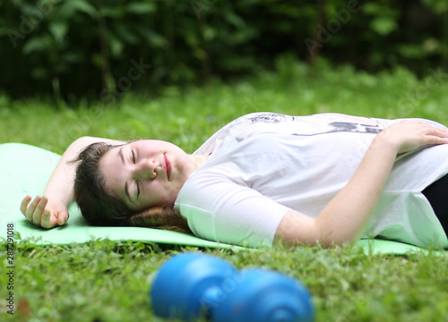 teenager girl lay exhausted on gym rag with dumbbell after train exercises