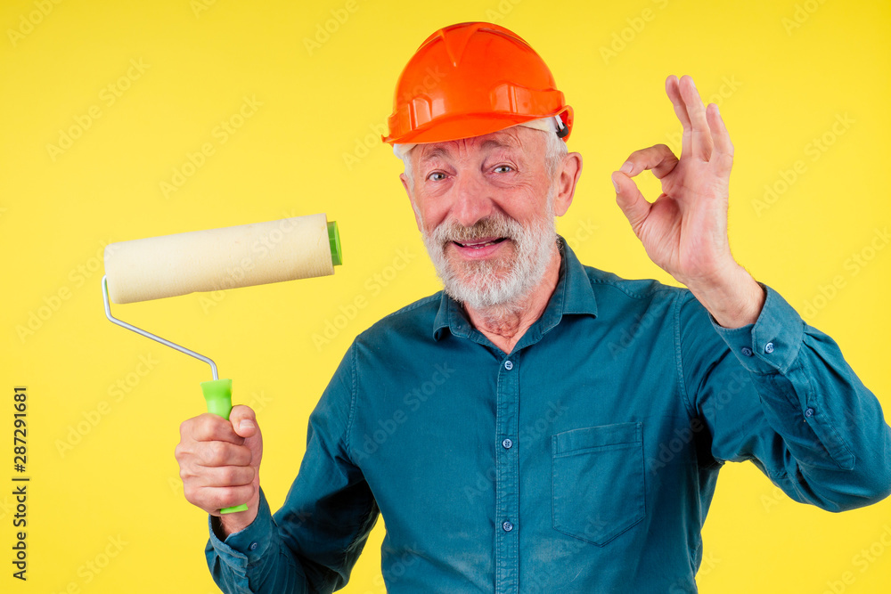Elderly handsome painting the walls in new a new house with yellow paint,holding roller brush,studio nackground.showing ok gesture Elderly handsome painting the walls in new a new house with yellow paint,holding roller brush,studio nackground.showing ok gesture