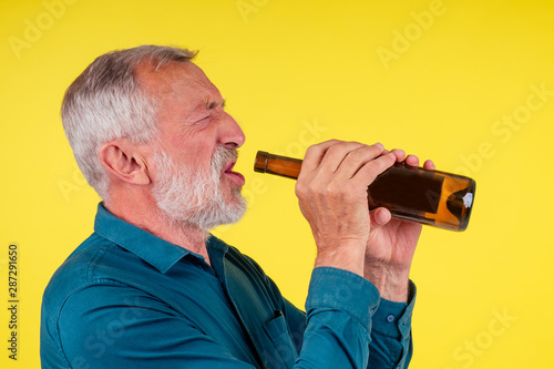 senior man drinking alcohol alone studio yellow baclground